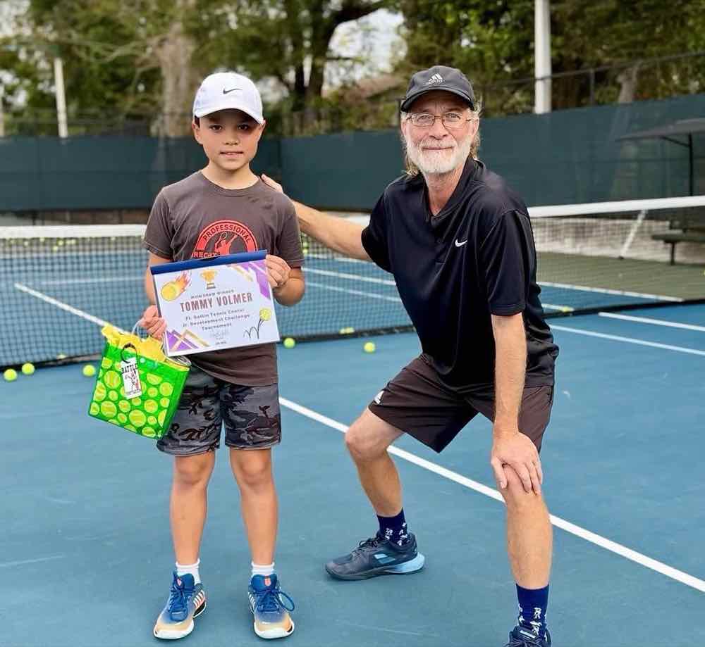 Coach Dave Walker on court with a junior tournament winner holding his certificate